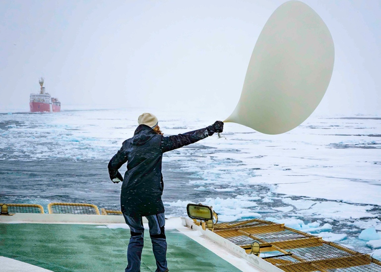 Doktorand står på däck och håller i stor ballong som rör sig i blåsten.