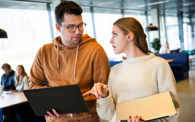 Manlig och kvinnlig student går och tittar och pekar på laptopskärm och diskuterar. 