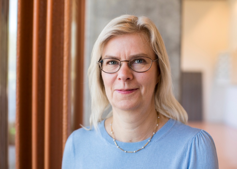 Gunilla Svensson står utomhus vid ett stort fönster,och hon speglas i profil i fönstret.