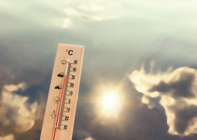 Termometer hååls upp mot himmel med sol och moln.