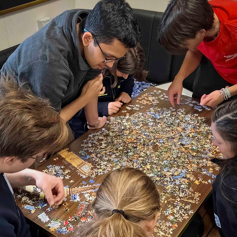 Students bending over a tale jammed with puzzle pieces.