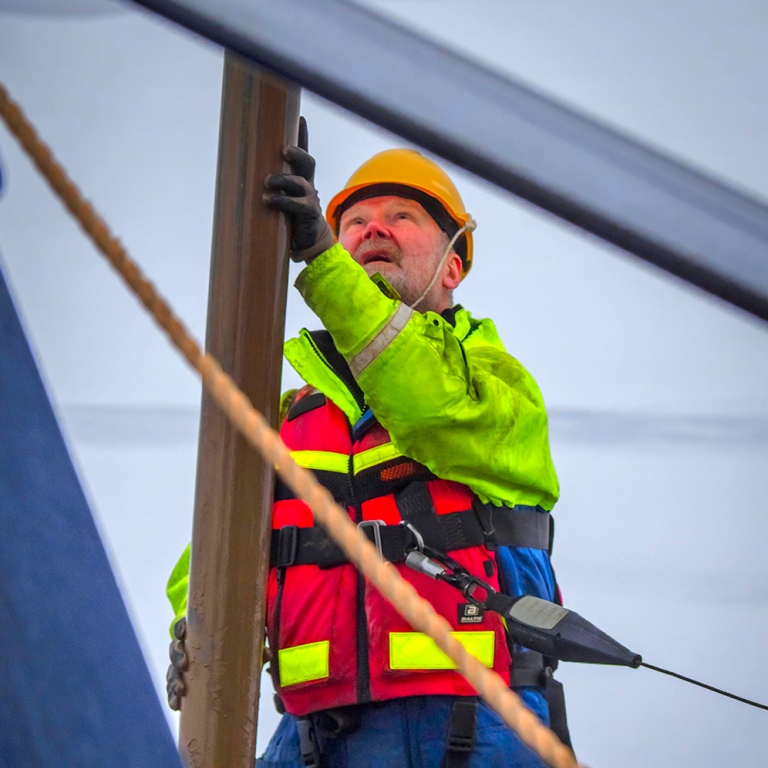 A man in lifewest, safety belt and helmet holding the sediment core.