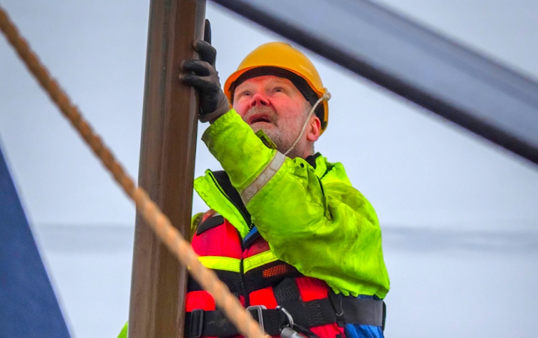 A man in lifewest, safety belt and helmet holding the sediment core.