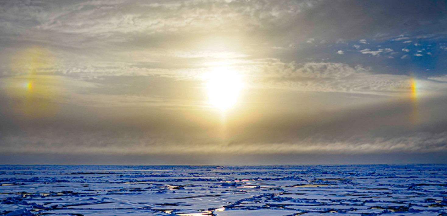 Cloudy sky, blue ice, bright sun, "sundogs" to the left and right, rainbow coloured.