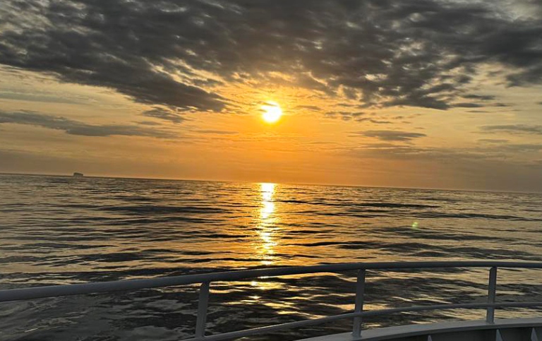 Sunset over the Atlantic Ocean. Ship railing in the foreground.
