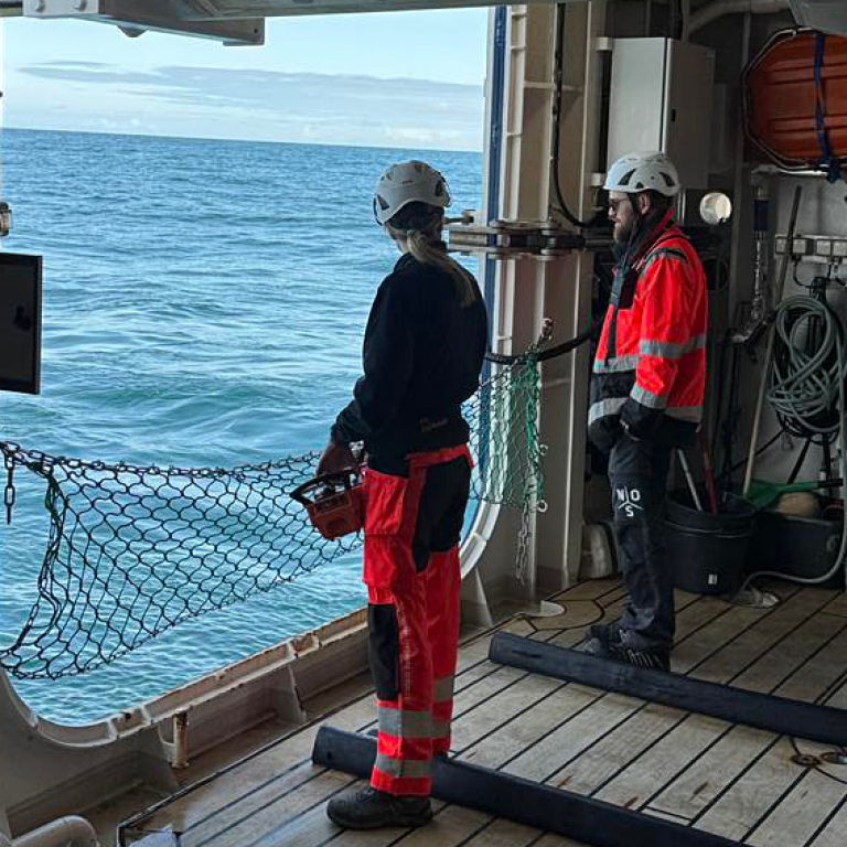 Two persons in helmets and protective clothes looking out on the Atlantic through a side port.