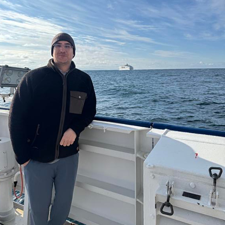 Léon Chafik standing by the railing on deck on RV Skagerak. Water and a ship in the background.
