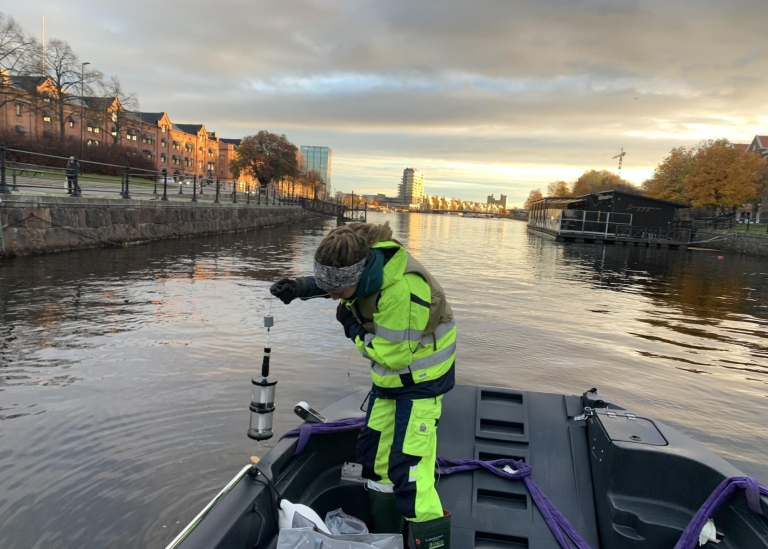 En kvinna i gula skyddskläder står i en båt