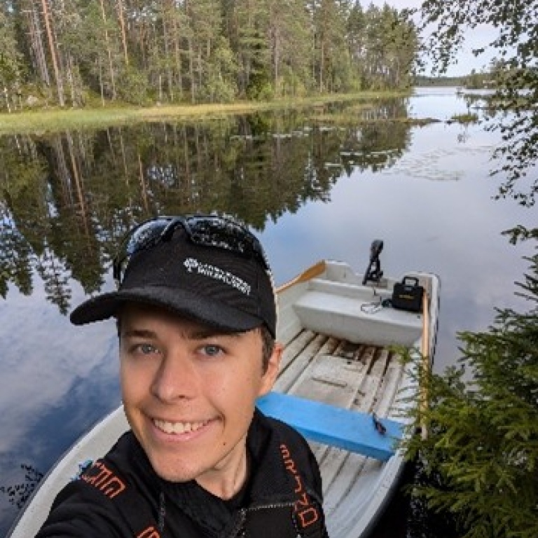En leende man med keps står vid en båt