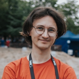 Mateusz wears a red shirt, round glasses, he has blue eyes, pale skin, and dark brown hair