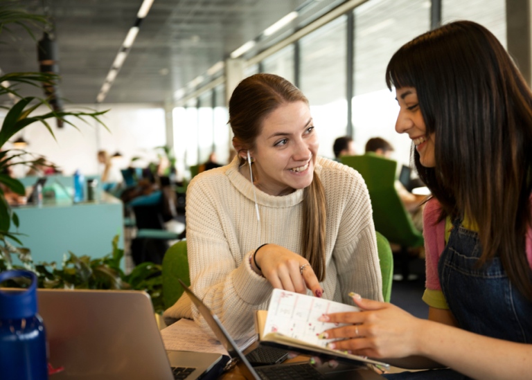 Two female smiling students sitting and studying together.
