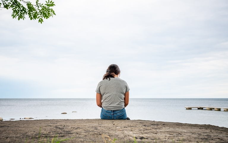Kvinna sedd bakifrån på en klipphäll tittar ut över havet.