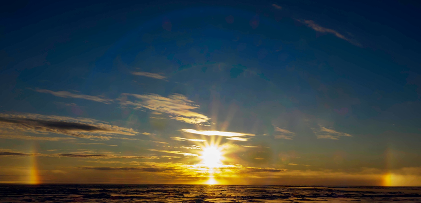 The sun, golden and darkblue sky and clouds, halo, sundogs, water.