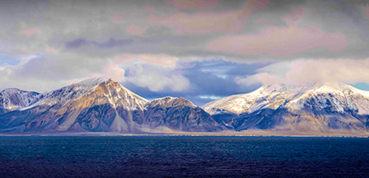 Mountains with snow tops, low clouds and the sun shining through,