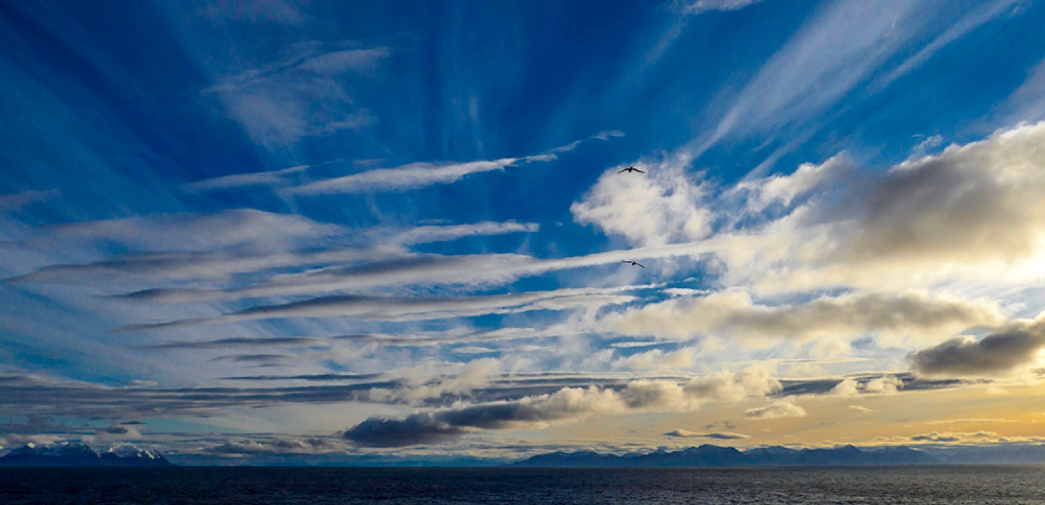 Mixed clouds in different directions, some reflecting the sunshine, blue sky, water.