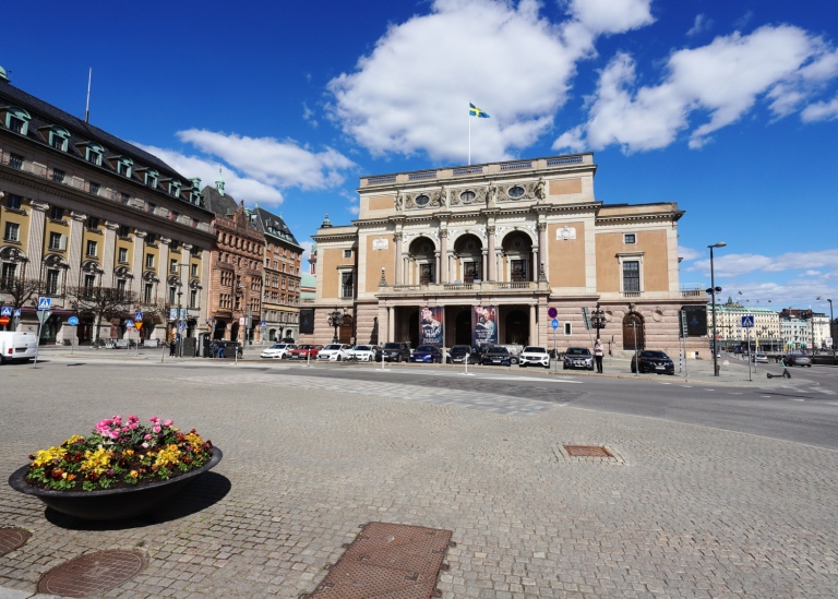 Exteriör av Kungliga Operan i Stockholm en solig dag, med svenska flaggan på taket.