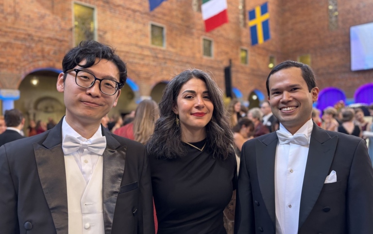 Tre personer poserar i högtidskläder under promotionshögtiden i Stadshuset.