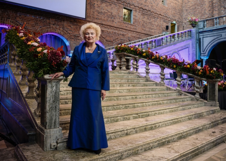 Kvinna i blå aftonklänning poserar i stentrappa vackert dekorerad med höstblommor..