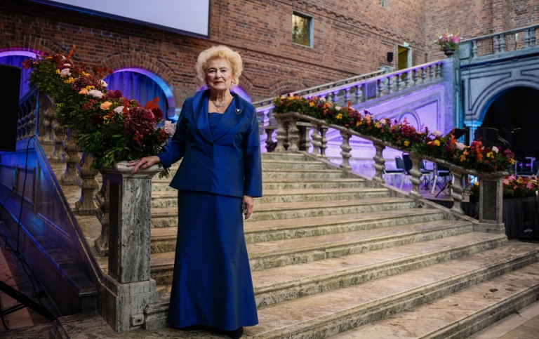 Kvinna i blå aftonklänning poserar i stentrappa vackert dekorerad med höstblommor..