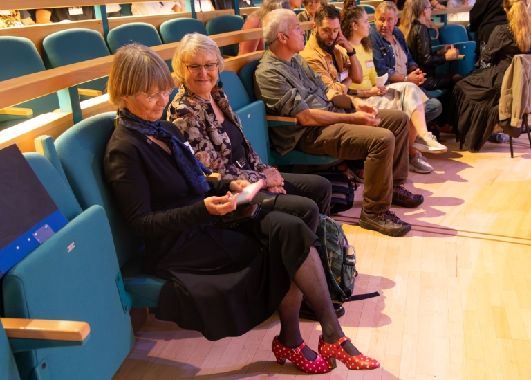 Två kvinnor sitter i en bänkrad i en aula