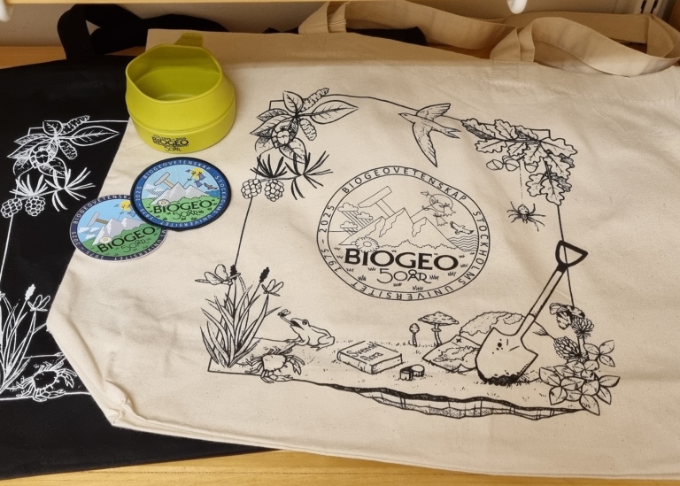 En tygkasse, dekaler och och en kåsa med BioGeo 50 år-symbolen