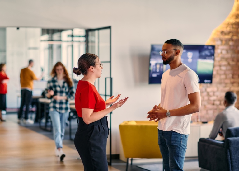 Two people having a conversation at a networking event, with others talking in the background.