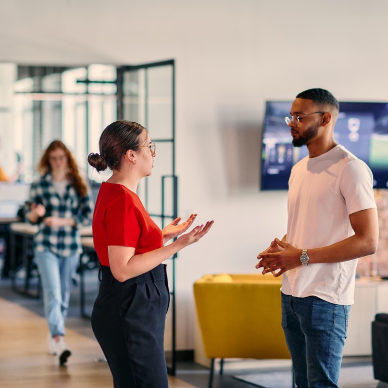 Two people having a conversation at a networking event, with others talking in the background.