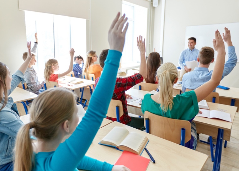 Elever i klassrum som räcker upp händerna,