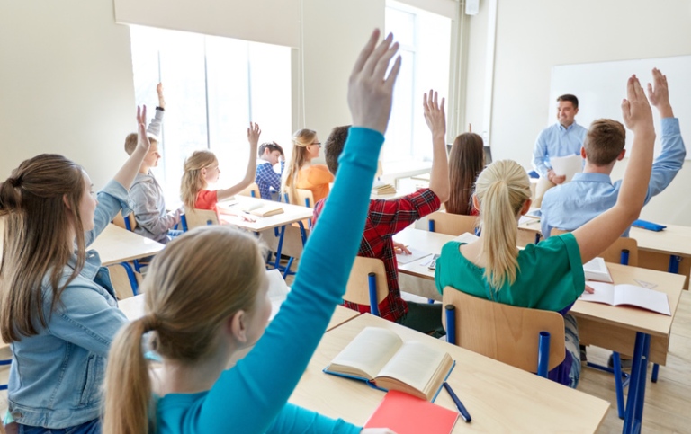 Elever i klassrum som räcker upp händerna,