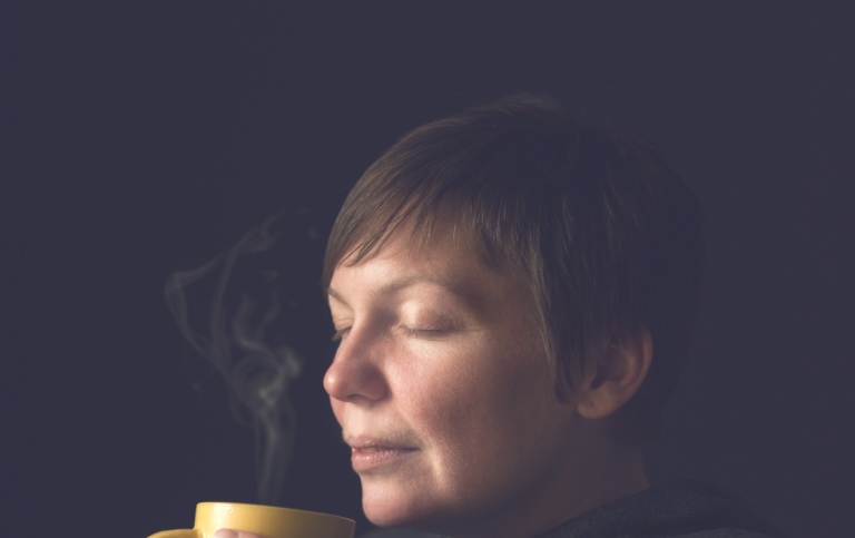 Person med kopp i händerna som luktar på kaffe