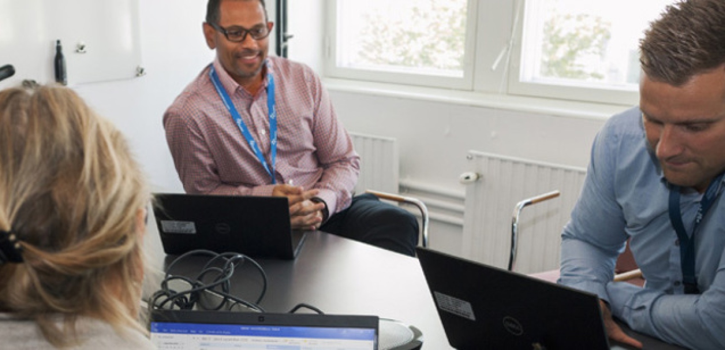 Fyra personer sitter vid ett onferensbord med laptoppar och pratar.