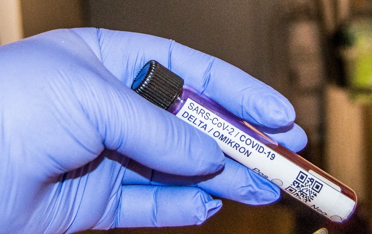 A hand with a blue glove holding a test tube with a Delta / Omikron COVID19-test.
