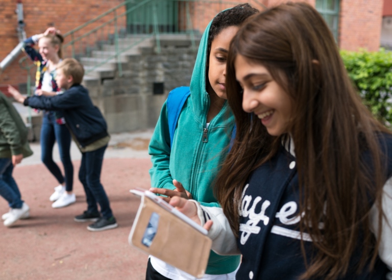 Mellanstadiebarn på skolgård med mobiltelefoner.