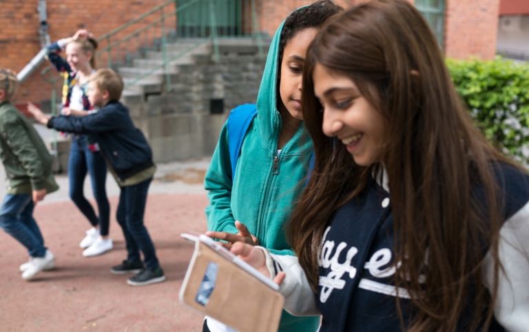 Mellanstadiebarn på skolgård med mobiltelefoner. 