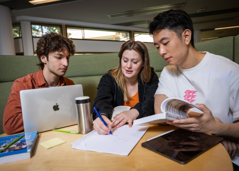Tre studenter sitter och arbetar vid ett bord tillsammans.
