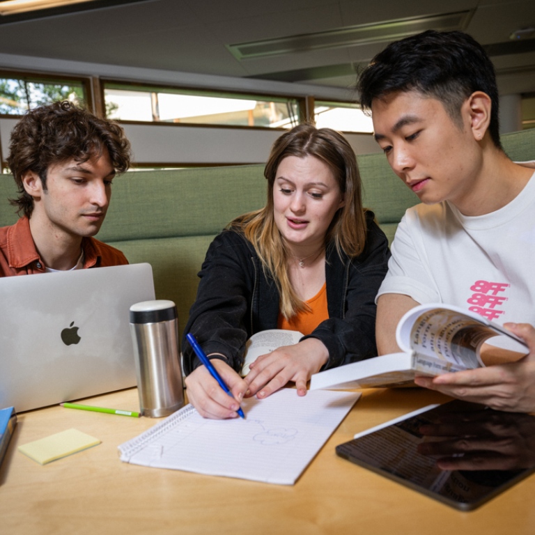 Tre studenter sitter och arbetar vid ett bord tillsammans.
