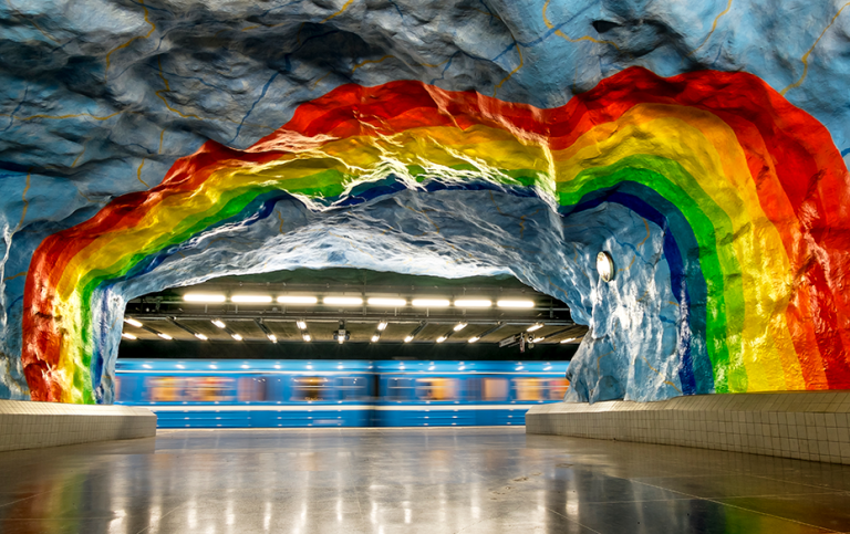 Tunnelbaneperrong med konstverk målat i taket som föreställer en regnbåge.