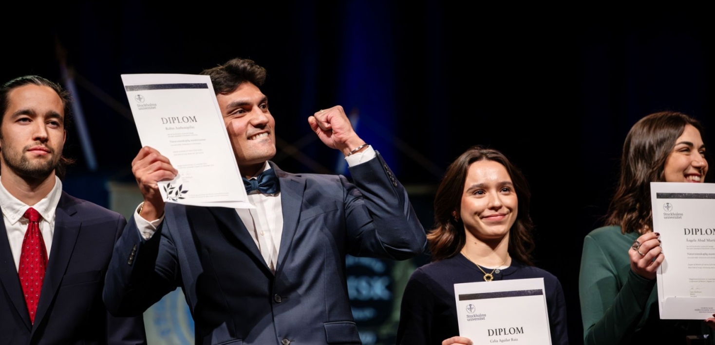 Studenter håller upp sina diplom på scenen under magisterpromotionen. 