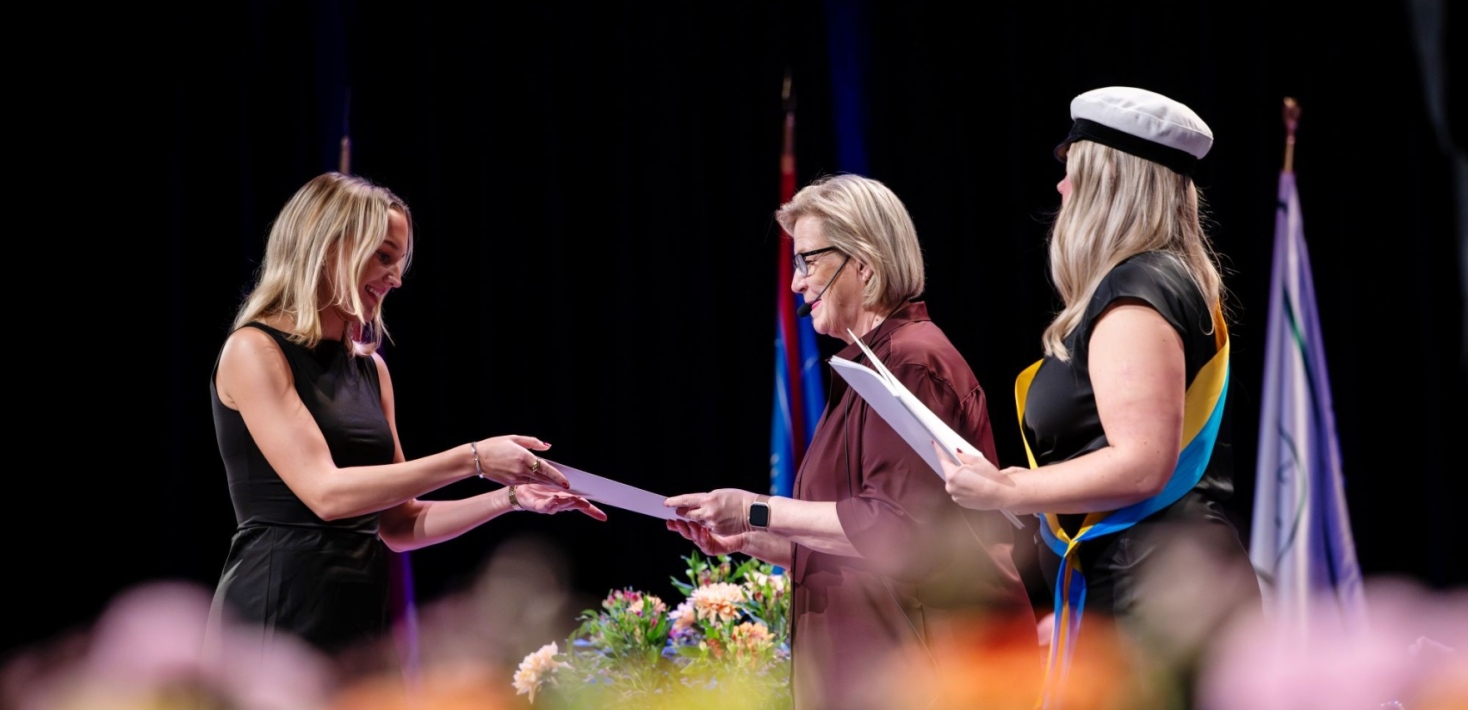 A student receives a diploma on stage from two people during the master's graduation ceremony.
