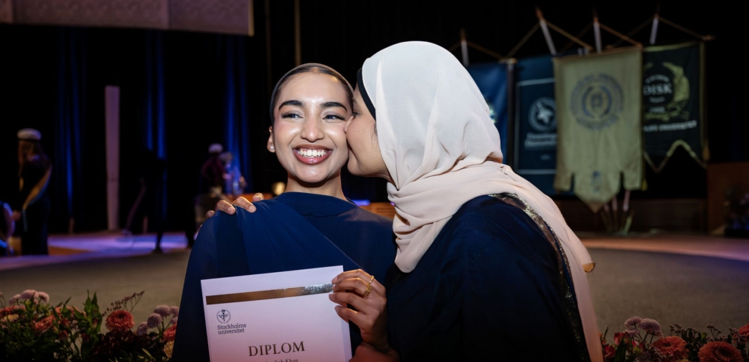 A person holds a diploma while another person congratulates with a gesture of closeness. 