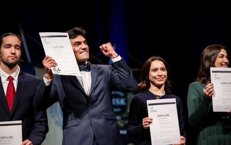 Students hold up their diplomas on stage during the master's graduation ceremony. 