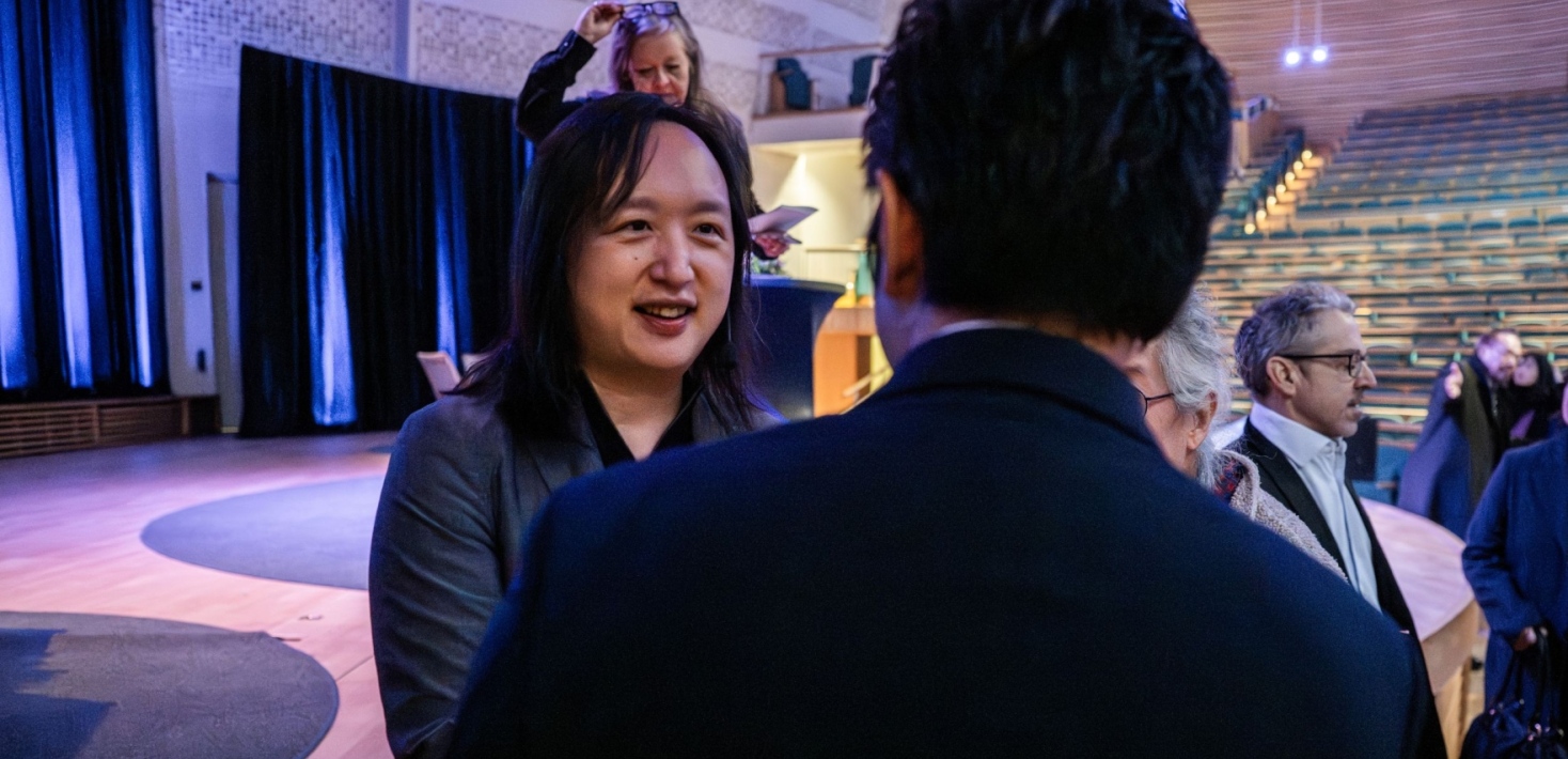 Audrey Tang i samtal med man i kostym framför scenen i Aula Magna